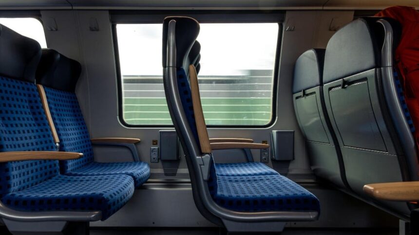 Interior de trem moderno com assentos azuis vazios e paisagem borrada pela janela.