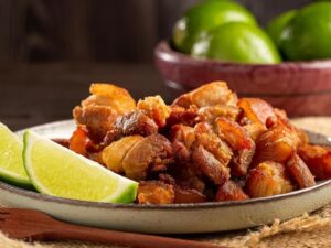 Torresmo frito crocante em prato com fatias de limão e limões frescos no fundo.