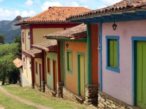 Fileira de casas coloniais coloridas em ladeira com telhados de barro e montanhas verdes ao fundo.
