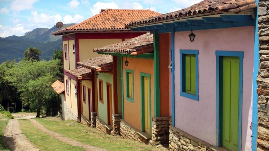 Fileira de casas coloniais coloridas em ladeira com telhados de barro e montanhas verdes ao fundo.