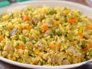 Tigela de galinhada vegana com arroz amarelo, cenoura, ervilha, salsão e pedaços de substituto de carne.