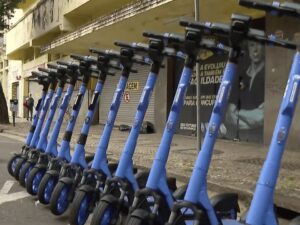 Dezenas de patinetes elétricos azuis e pretos alinhados em rua de Belo Horizonte.