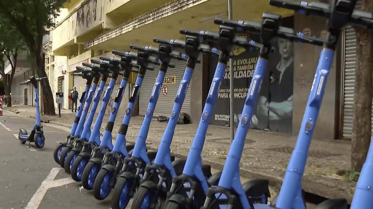 Dezenas de patinetes elétricos azuis e pretos alinhados em rua de Belo Horizonte.