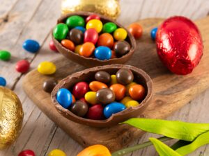 Ovos de Páscoa de chocolate abertos com doces coloridos e ovos embrulhados sobre superfície de madeira.