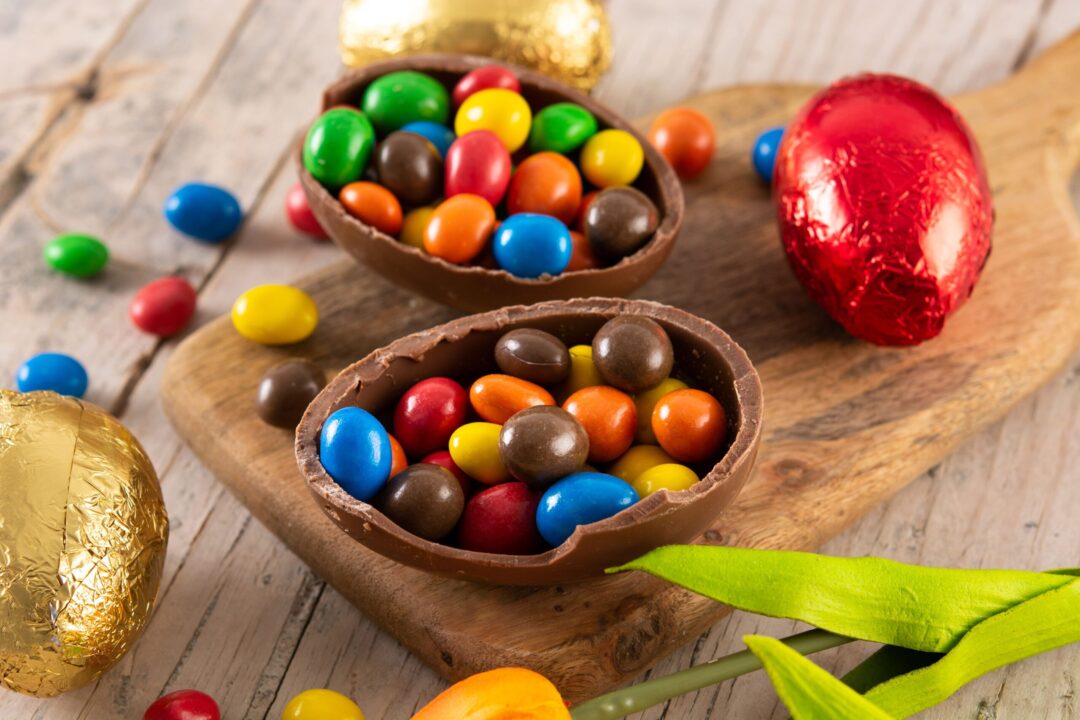 Ovos de Páscoa de chocolate abertos com doces coloridos e ovos embrulhados sobre superfície de madeira.