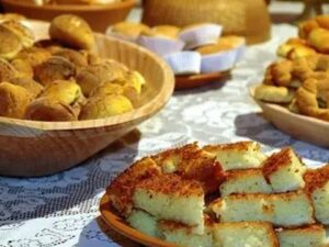 Mesa com broas em tigelas de madeira e bolo de fubá cortado em quadrados sobre um prato.