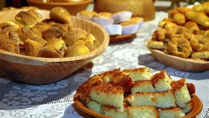 Mesa com broas em tigelas de madeira e bolo de fubá cortado em quadrados sobre um prato.