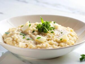 Tigela branca com risoto cremoso, pedaços de queijo, salsinha fresca e pimenta do reino moída.