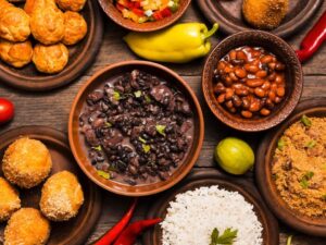 Comida brasileira em mesa de madeira: feijão, arroz, farofa, salgados, pimentas e legumes.
