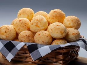 Cesta de vime cheia de pão de queijo dourado com pano xadrez preto e branco.
