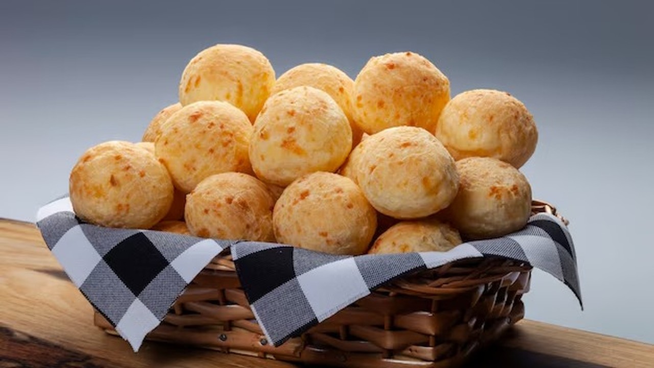 Cesta de vime cheia de pão de queijo dourado com pano xadrez preto e branco.