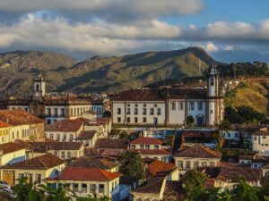 Vista panorâmica de cidade histórica com edifícios brancos, telhados de cerâmica vermelha e montanhas ao fundo.