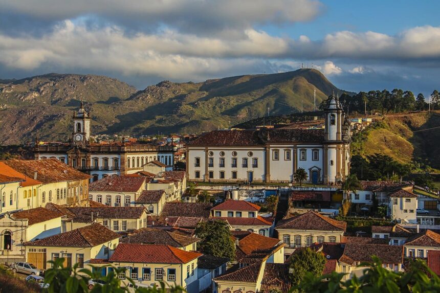 Vista panorâmica de cidade histórica com edifícios brancos, telhados de cerâmica vermelha e montanhas ao fundo.