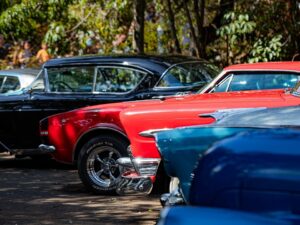 Fileira de carros clássicos coloridos, vermelho, preto e azul, em exposição ao ar livre.