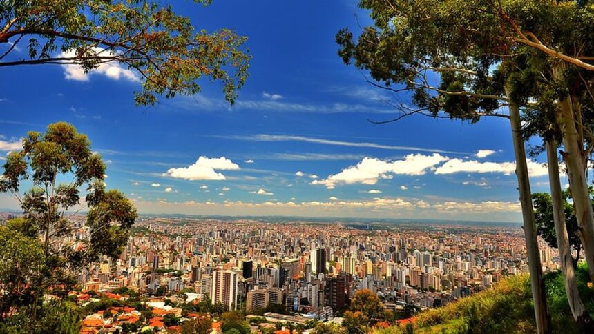 Vista panorâmica da cidade de Belo Horizonte com prédios, céu azul e nuvens, emoldurada por árvores.