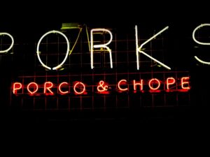 Letreiro neon com a palavra "PORKS" em branco e "PORCO & CHOPE" em vermelho.