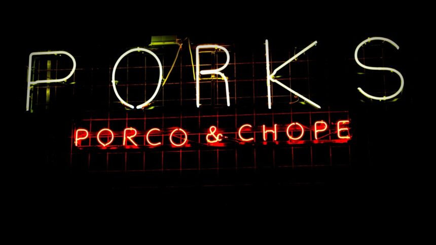 Letreiro neon com a palavra "PORKS" em branco e "PORCO & CHOPE" em vermelho.