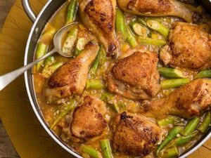 Frango com quiabo em panela, com colher, sobre base de madeira e dourada.