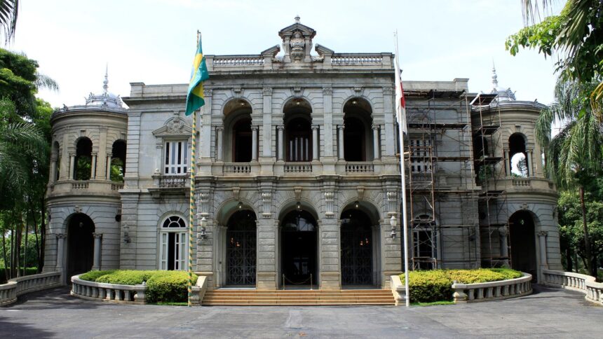 Fachada do Palácio da Liberdade em Belo Horizonte, com arcos, colunas, bandeiras e andaimes à direita.