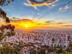 Vista panorâmica da cidade de Belo Horizonte ao pôr do sol, com muitos prédios e árvores.