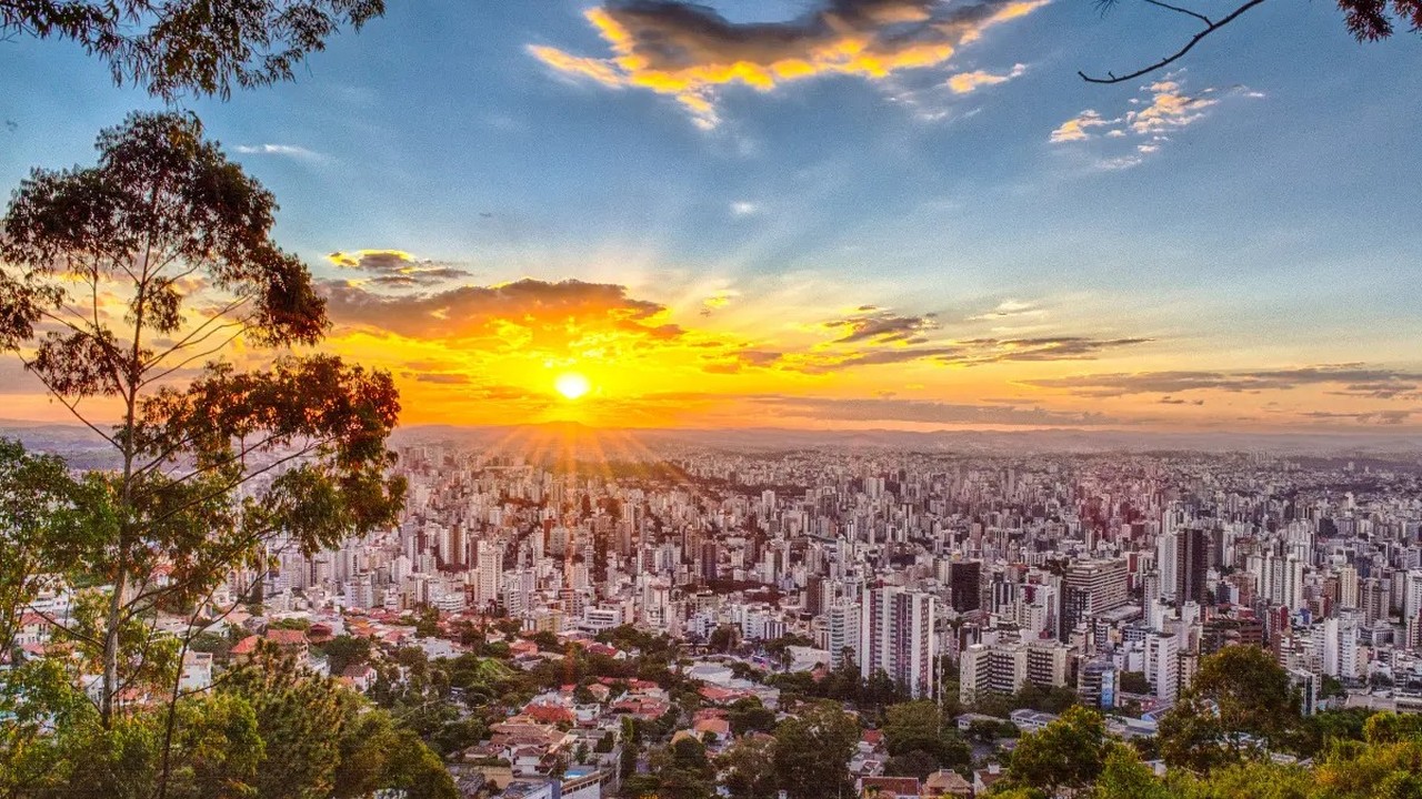 Vista panorâmica da cidade de Belo Horizonte ao pôr do sol, com muitos prédios e árvores.