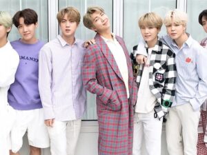 Sete membros do grupo musical BTS posam em fila, vestindo roupas casuais.