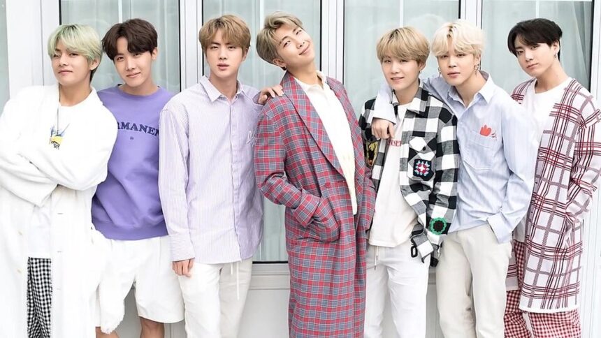 Sete membros do grupo musical BTS posam em fila, vestindo roupas casuais.