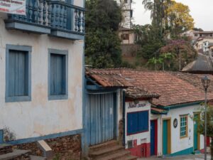 Rua de paralelepípedos ladeada por casarões coloniais brancos, azuis e coloridos com telhados de cerâmica.