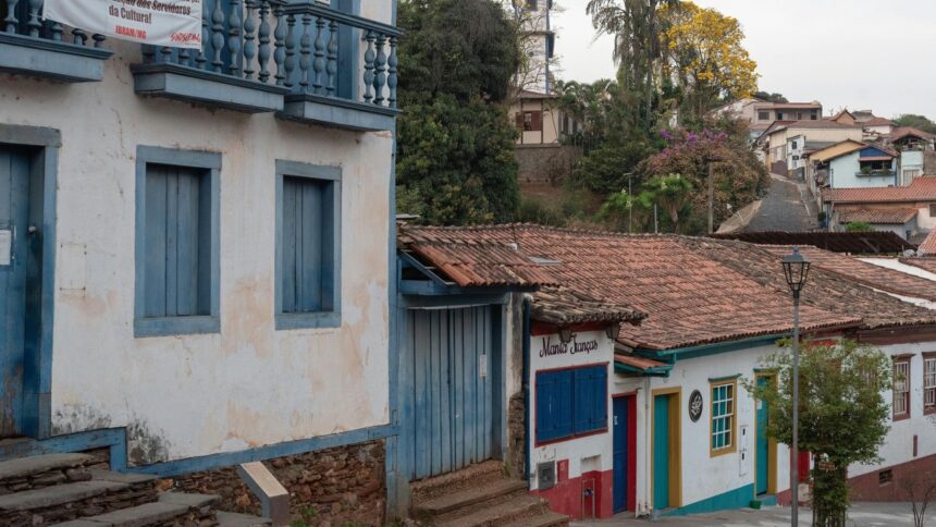 Rua de paralelepípedos ladeada por casarões coloniais brancos, azuis e coloridos com telhados de cerâmica.