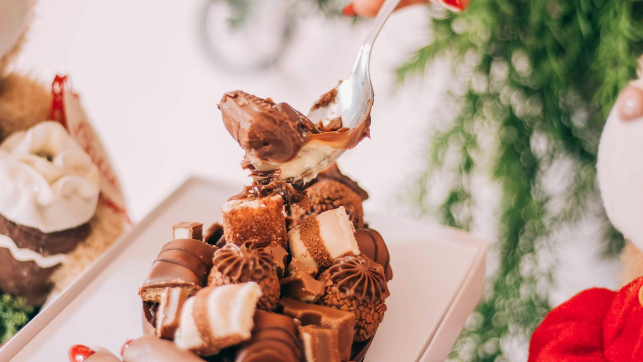 Mão com colher tirando recheio cremoso de ovo de Páscoa com chocolates e bombons.