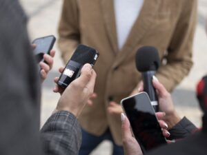 Mãos seguram microfones e smartphones registrando áudio e vídeo em uma entrevista.