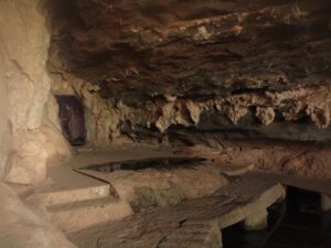 Interior de caverna rochosa com estalactites, degraus esculpidos e poça escura