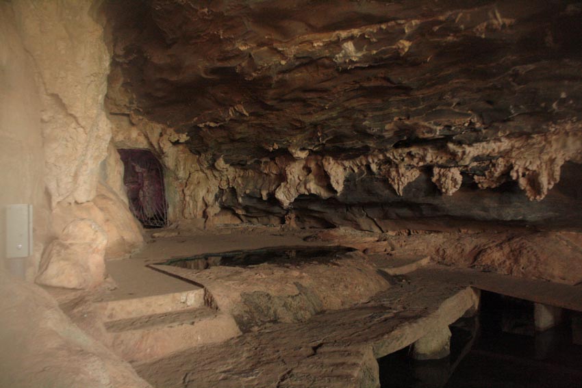 Interior de caverna rochosa com estalactites, degraus esculpidos e poça escura