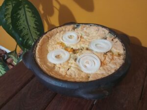 Torta capixaba caseira em panela de barro escura com quatro rodelas de cebola