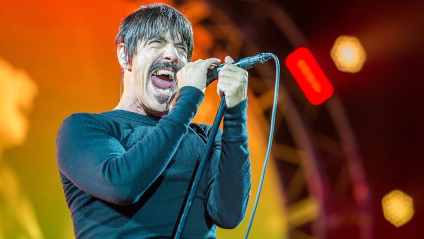 Anthony Kiedis, vocalista, canta intensamente no microfone em palco iluminado por luzes quentes.