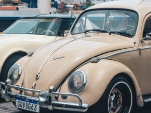 Volkswagen Fusca bege e Corvette creme antigos expostos em evento automotivo.