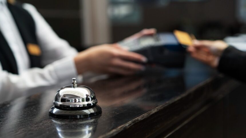 Campainha de recepção em primeiro plano e, ao fundo, mãos passando cartão de crédito na máquina.