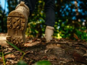 Sola de uma bota de trekking bege pisando em caminho de terra com folhas secas.