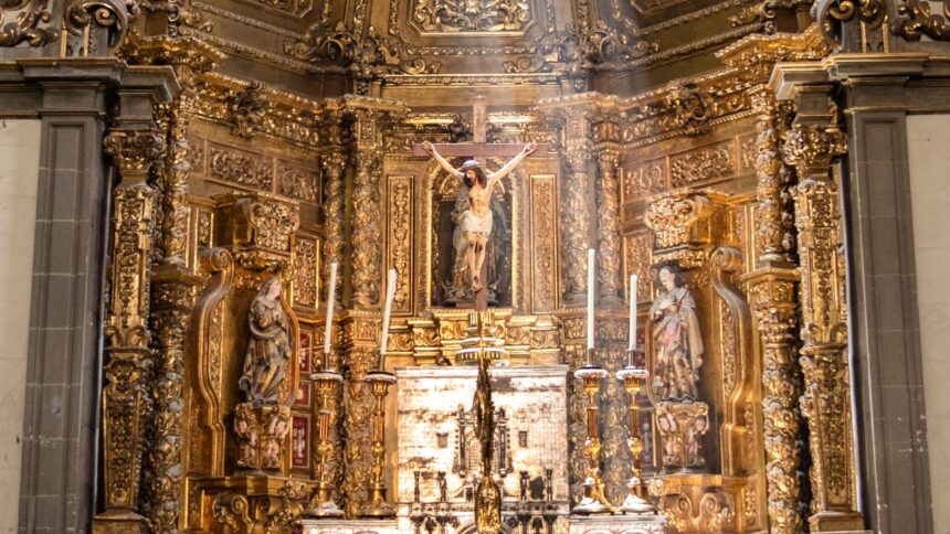 Ornate golden Baroque church altar with a crucifix, statues of saints, and candles.