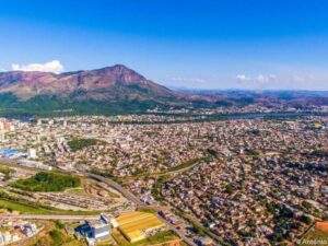 Vista aérea de uma cidade com montanha imponente, rio sinuoso e céu azul.