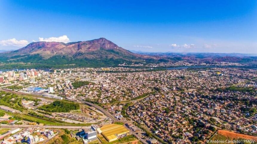 Vista aérea de uma cidade com montanha imponente, rio sinuoso e céu azul.
