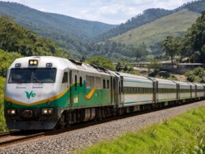 Trem de passageiros branco, verde e amarelo em trilhos, cercado por montanhas verdes.