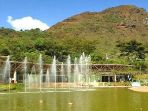 Lagoa com chafarizes, edifício moderno e montanhas no Parque Ecológico da Pampulha, BH.