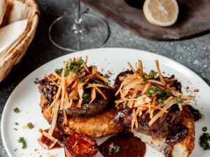 Dois medalhões de carne com molho, batata palha e cebolinha em prato branco digno de estrela Michelin