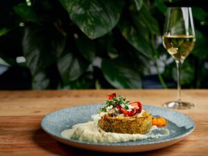 Prato gourmet com crosta dourada, molho branco, pimentões vermelhos e tomilho, em mesa de madeira