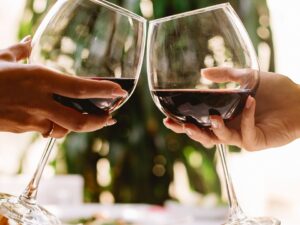 Duas mãos brindam com taças de vinho tinto em um restaurante.