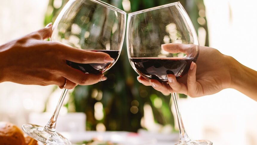 Duas mãos brindam com taças de vinho tinto em um restaurante.