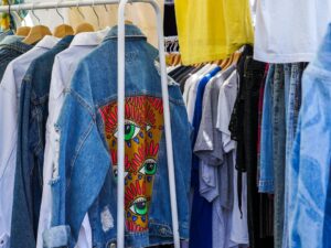 Variadas roupas penduradas em cabides, com destaque para uma jaqueta jeans azul decorada.