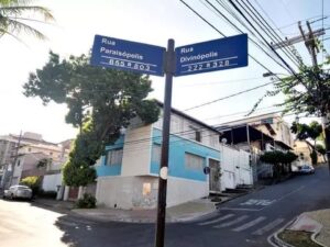 Sinal de rua azul com 'Rua Paraisópolis' e 'Rua Divinópolis', em esquina arborizada de BH.