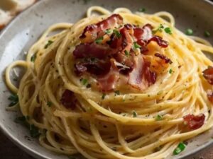 Espaguete cremoso com pedaços de bacon crocante e salsinha picada em um prato claro.